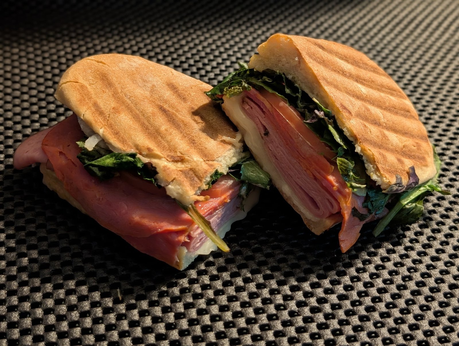 Fresh panini cut in half showing deli meat, melted cheese, tomato and greens